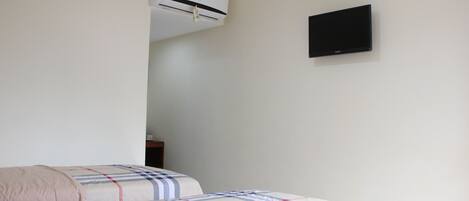 A bedroom with two beds, an air conditioner, and a flat-screen TV on the wall.