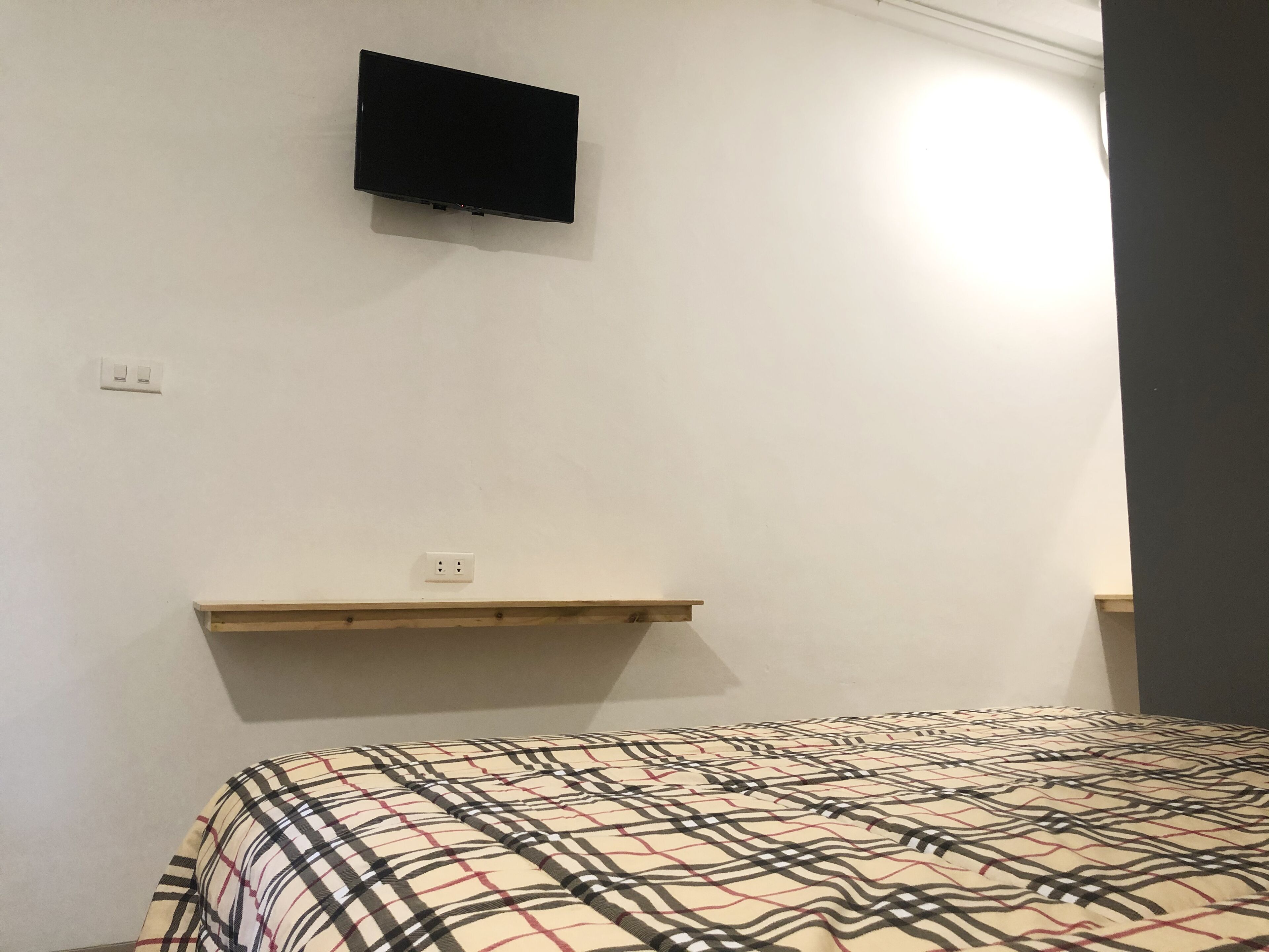 Une chambre à coucher avec un lit, un téléviseur fixé au mur et une étagère.