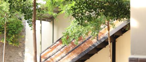 A staircase with wooden steps and metal railings, surrounded by greenery and a building facade.