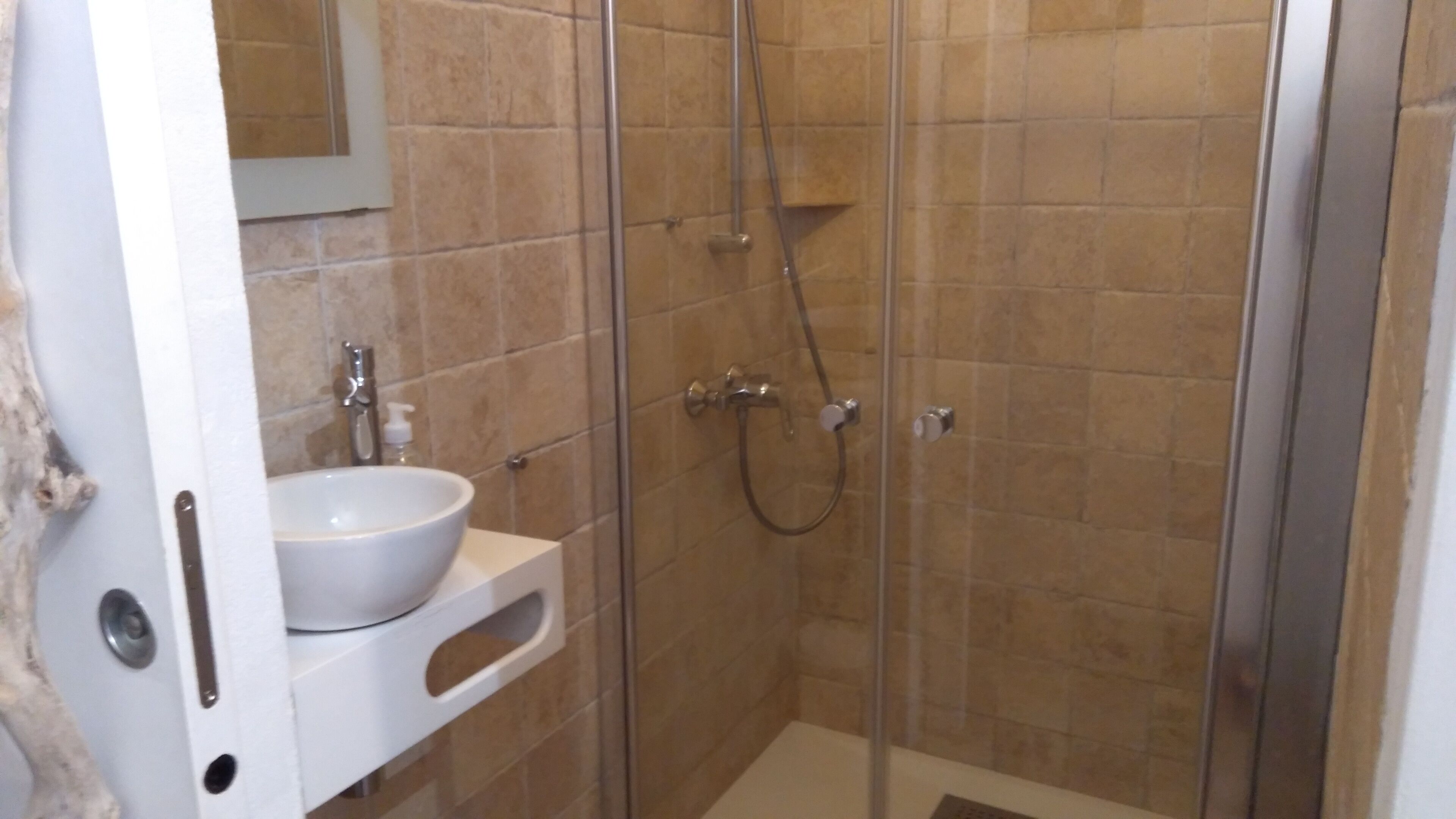 A bathroom with a glass-enclosed shower, a white sink, and a mirror.