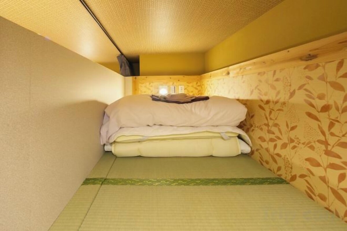 Una habitación pequeña y estrecha con una cama, una mesita de noche y un papel tapiz con diseño de hojas.