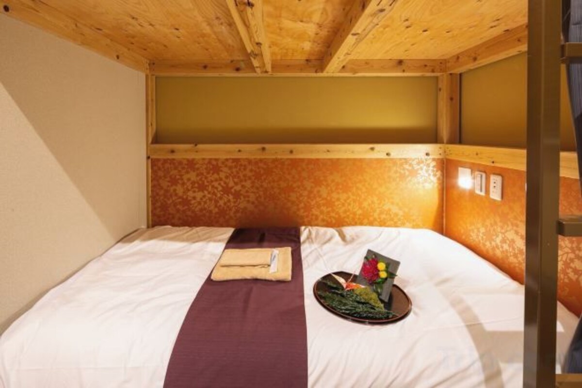 Una cama individual con cabecera de madera, una toalla doblada y una bandeja con frutas y una bebida.