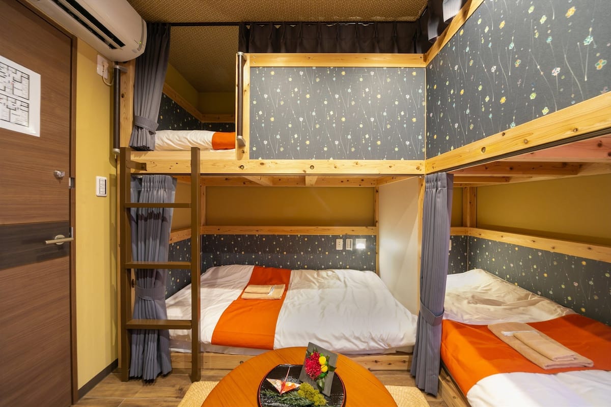 A bunk bed room with a wooden ladder, a small table with a flower arrangement, and a wall with a floral pattern.