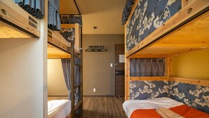 Een slaapkamer met stapelbedden, een houten vloer, een bed met oranje dekbed en een wand met bloemenbehang.