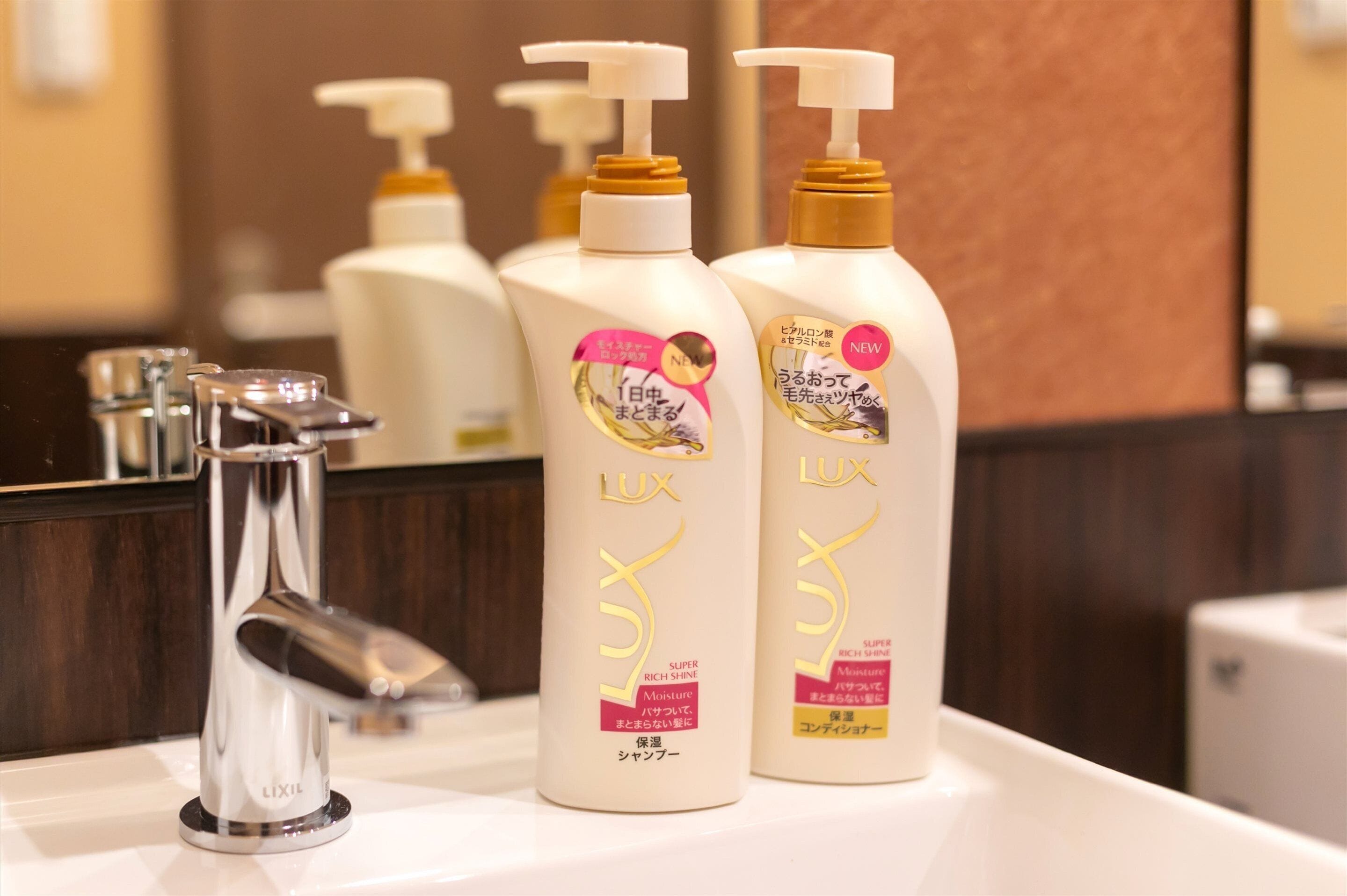 Ein Badezimmer mit einem modernen Wasserhahn und drei Flaschen Lux Shampoo auf der Ablagefläche.