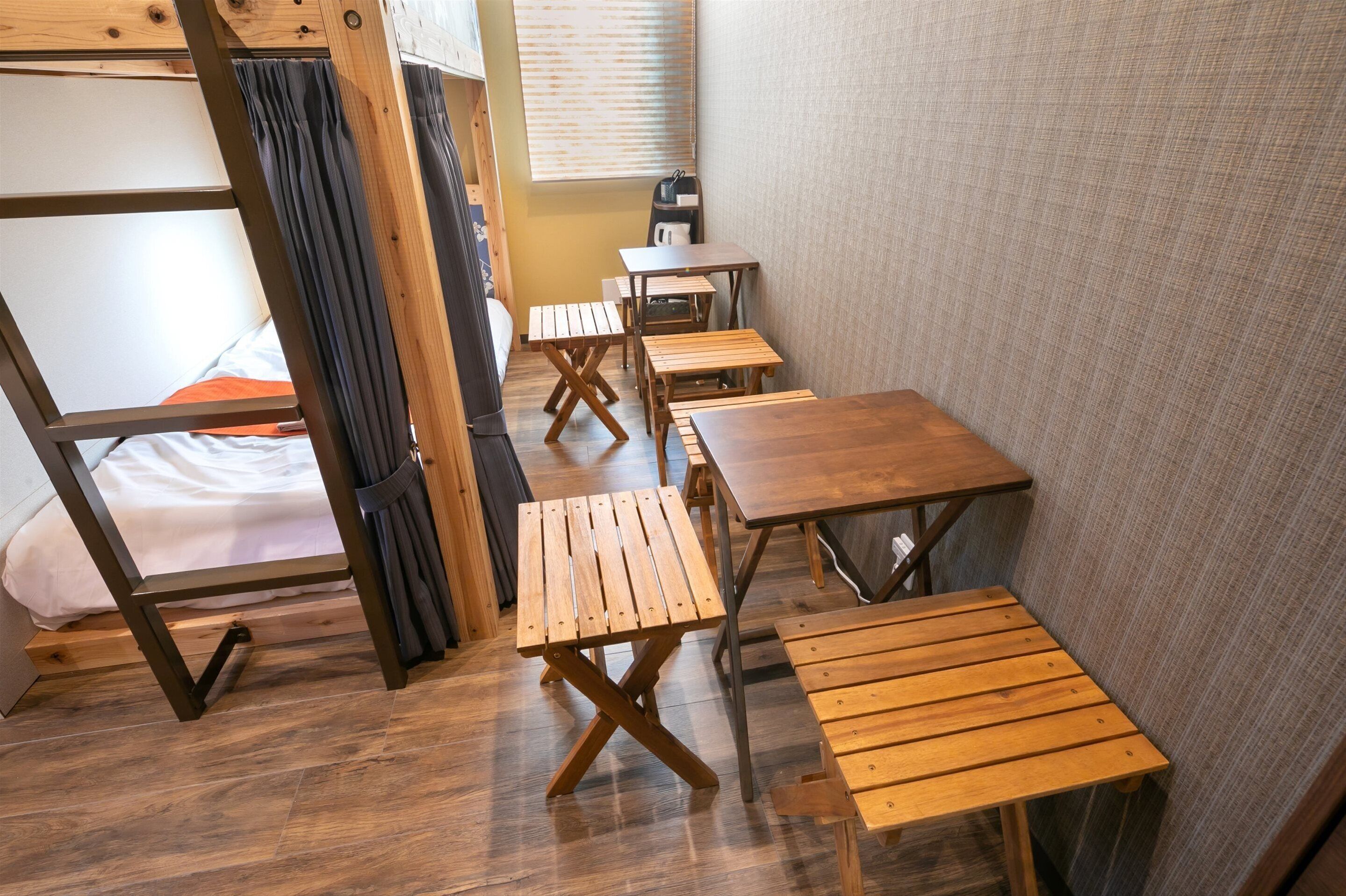 A dormitory room with bunk beds, wooden tables, and a small desk.
