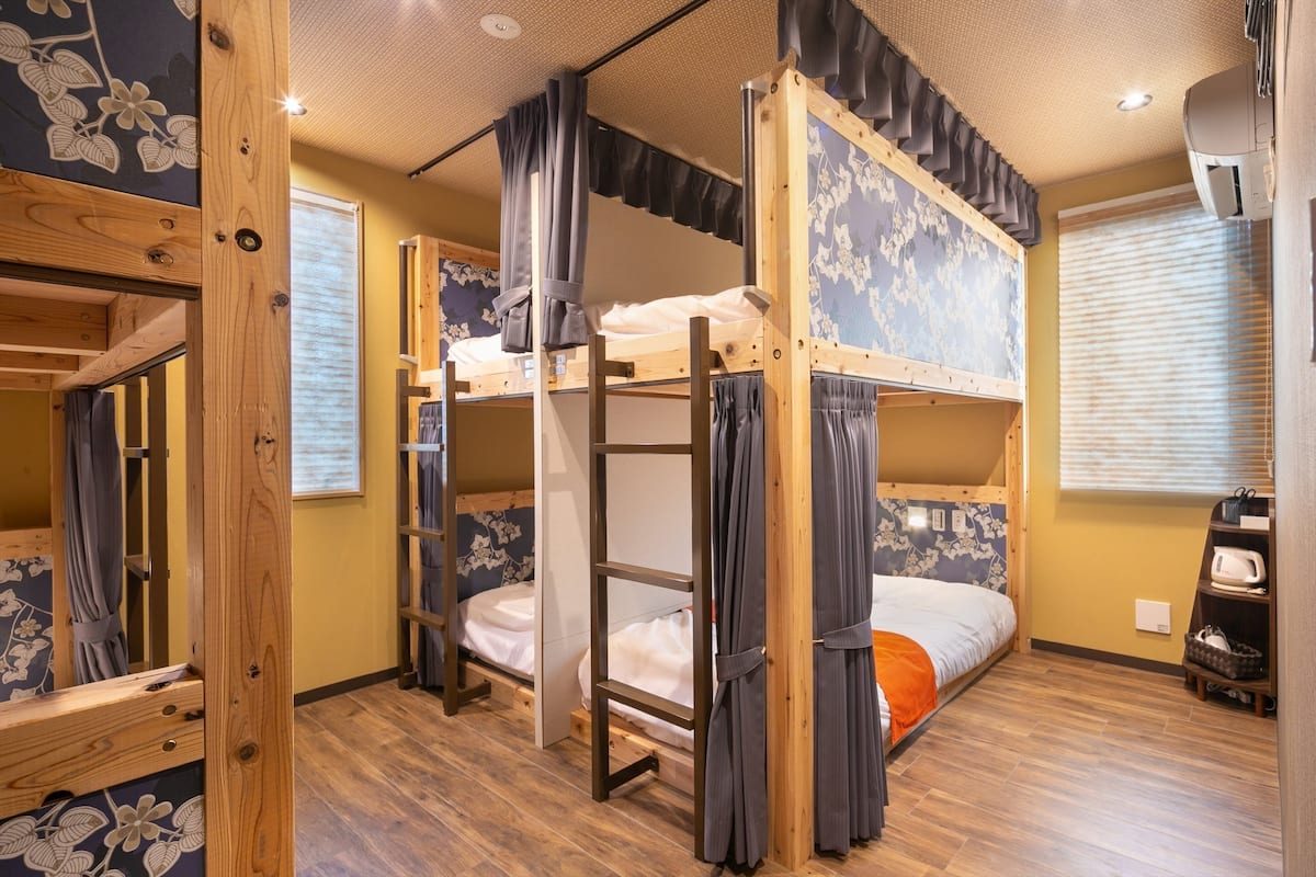 A bunk bed room with wooden frames, curtains, and a floral wallpaper design.