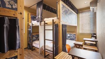 A bunk bed room with a wooden desk and a small table, curtains, and a wall with floral wallpaper.