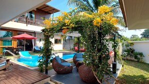 Ein Poolbereich im Freien mit Liegestühlen, einer Holzterrasse und einer überdachten Sitzgelegenheit mit Sonnenschirm.