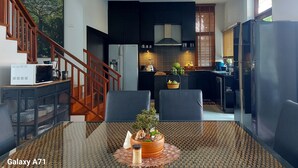 Eine moderne Küche mit dunklen Schränken, einem eingebauten Backofen und einem Kühlschrank. Es gibt einen Essbereich mit einem Glastisch und Stühlen, sowie eine Treppe mit Holzwandungen.