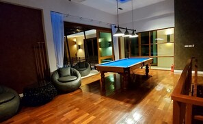 A billiards table in a room with wooden flooring, two black chairs, and a ceiling light fixture. - Private swimming pool and solar-heated rooftop mini pool with mountain and sea views (Prachuab Kirikhan)