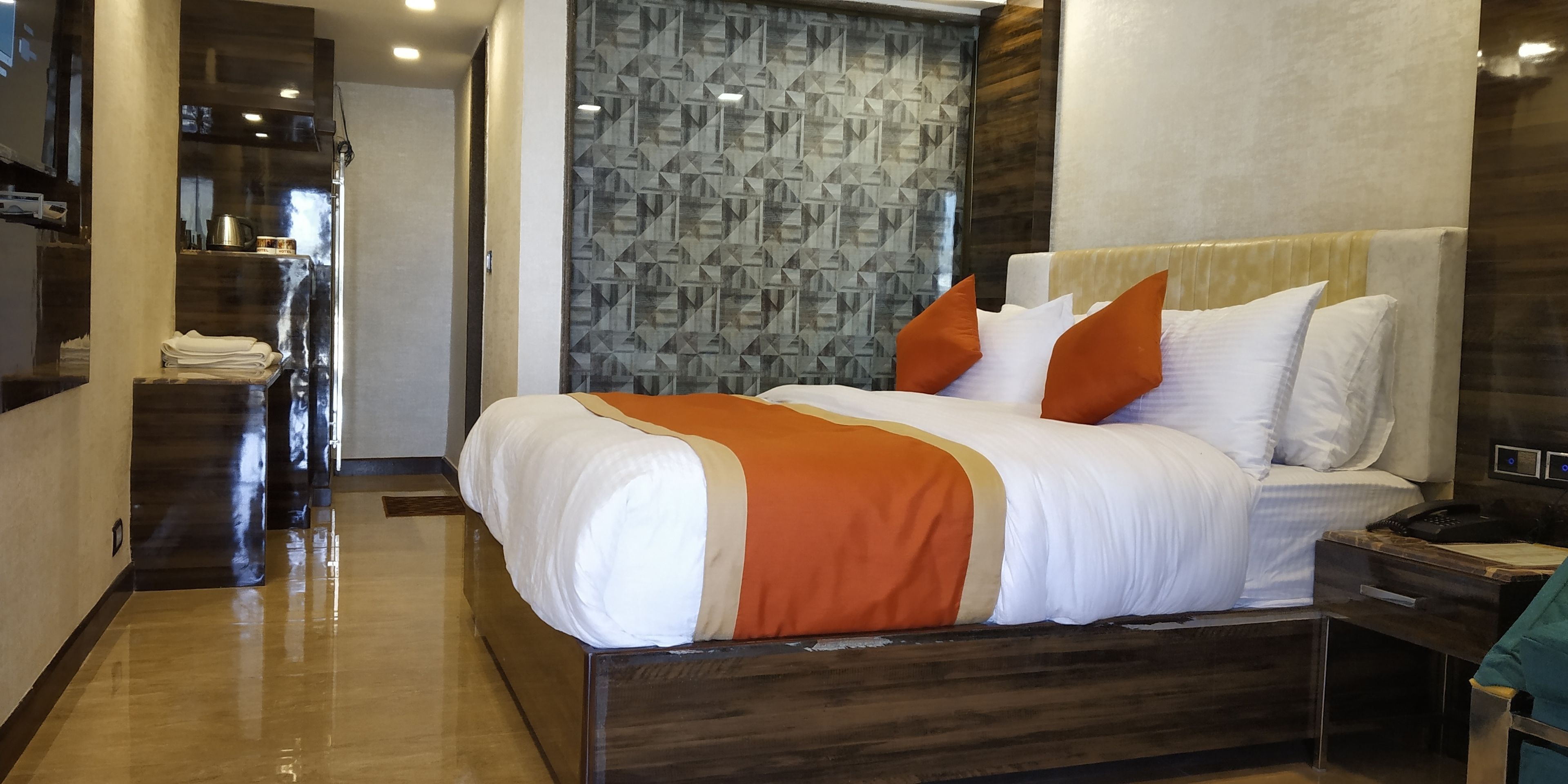 Une chambre d’hôtel moderne avec un grand lit, une tête de lit en bois et un mur orné d’un motif.