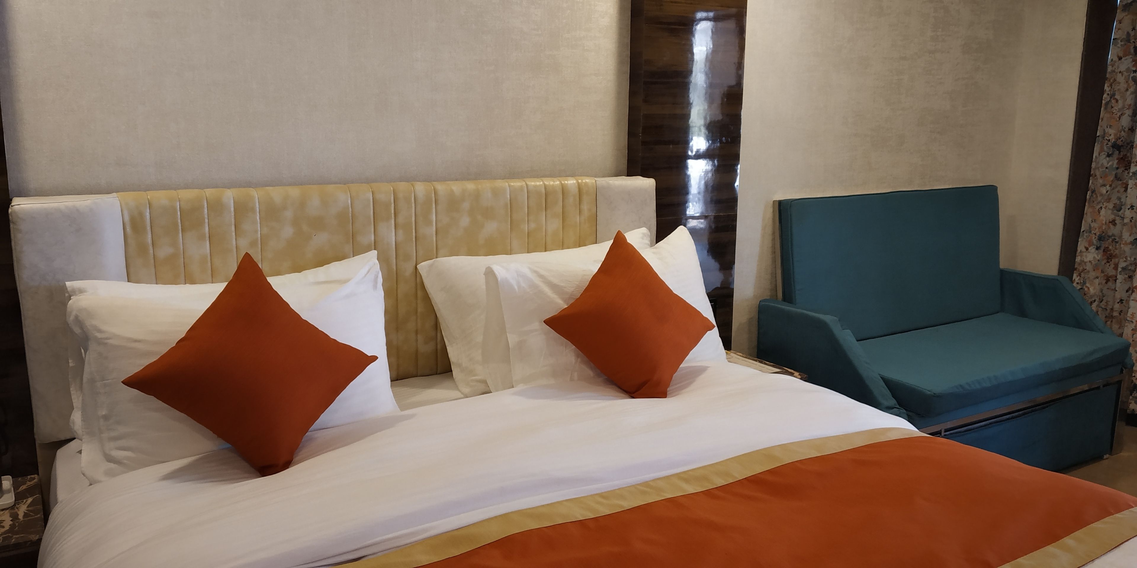 Una camera d'albergo con un letto, due cuscini, una poltrona blu e una testiera in legno.