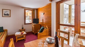 Una habitación acogedora con una pared de madera, una cama, una mesita con copas de vino, un televisor y una ventana con vistas a un paisaje nevado.