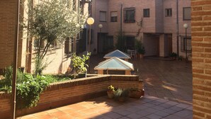A courtyard with brick buildings, a covered seating area, and potted plants.