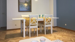 A dining area with a table set for four, white chairs, a yellow tablecloth, and a framed painting on the wall.