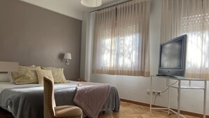 A hotel room with a bed, a chair, a TV on a stand, and a window with curtains.