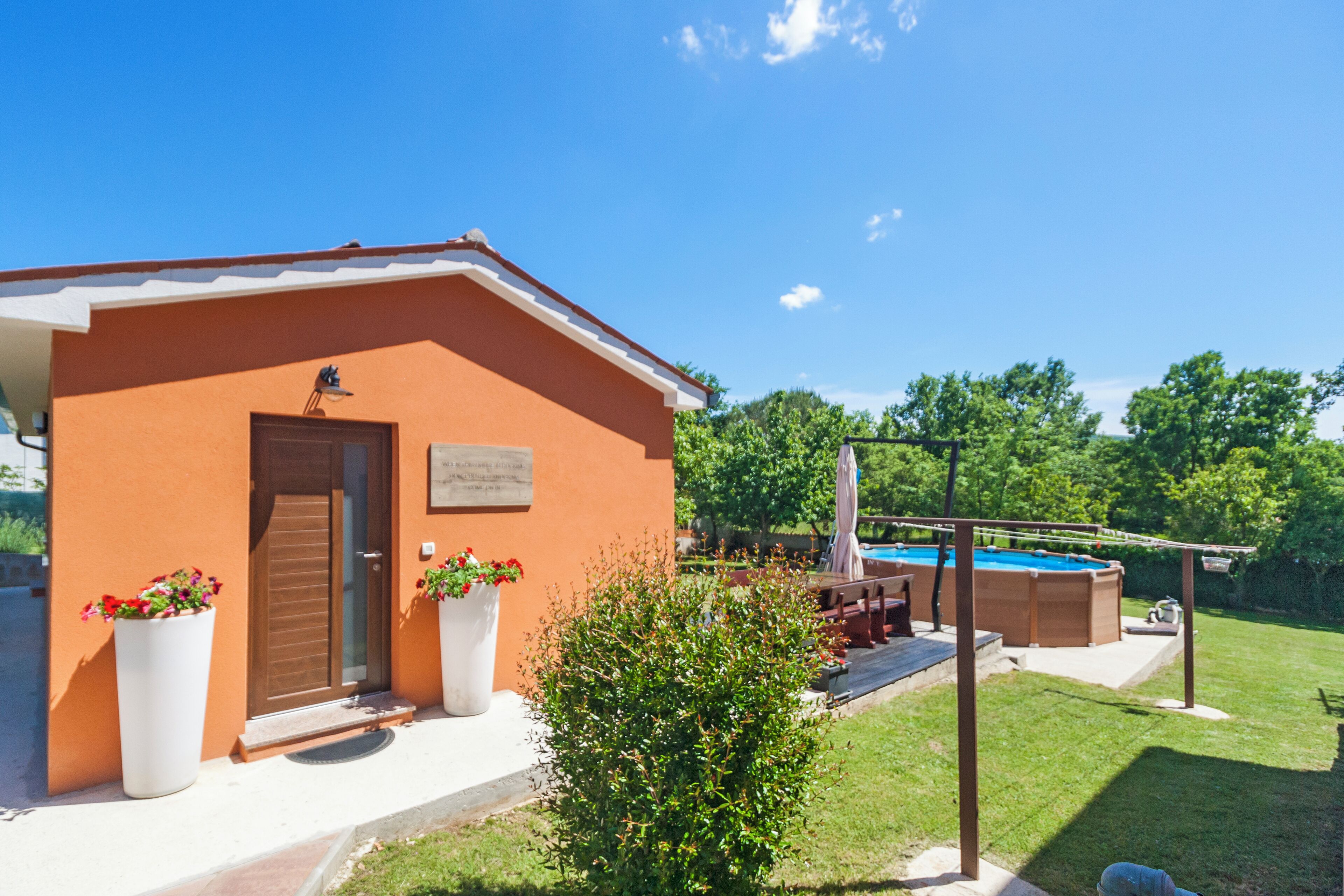 Un edificio con fachada marrón, una puerta y dos macetas grandes. Zona de piscina con tobogán y jacuzzi.