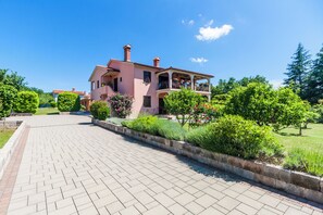 Een roze huis met een tuin en een verharde oprit.