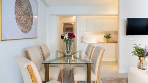 A dining area with a glass table and cushioned chairs, a vase with flowers, and a kitchen in the background. - Genteel Home Velarde II (Seville)
