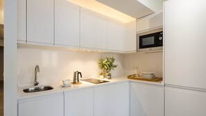A modern kitchen with white cabinetry, a stainless steel sink, a kettle, a microwave, and a small potted plant. - Genteel Home Velarde II (Seville)