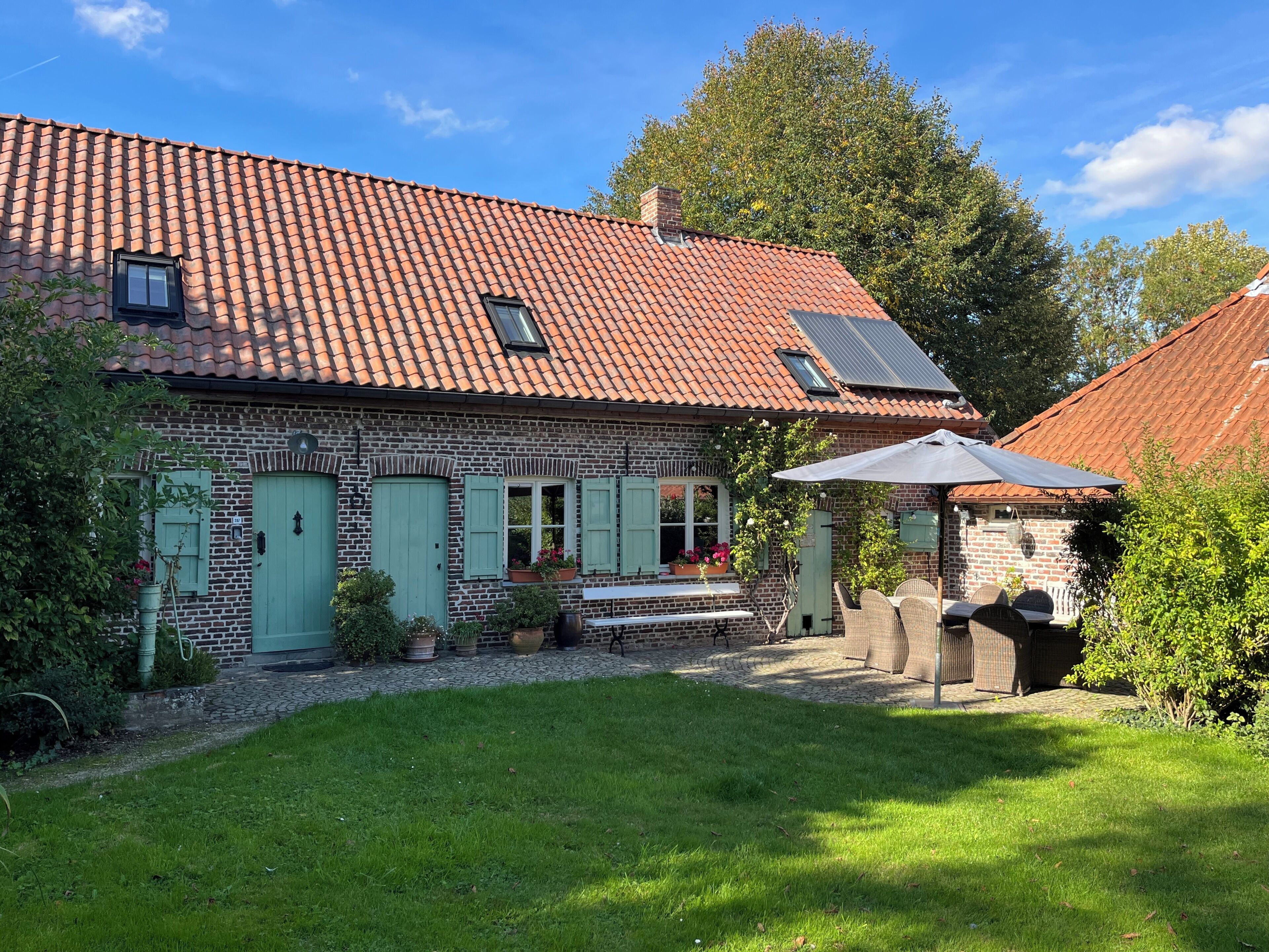 Een bakstenen huis met pannendak, een klein terras met tuinmeubilair en een tuin.