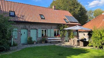Een bakstenen huis met pannendak, een klein terras met tuinmeubilair en een tuin.