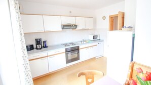 Une cuisine de taille réduite avec des meubles blancs, un four à micro-ondes, une cuisinière et un lave-vaisselle.