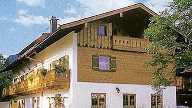 Une maison traditionnelle à deux étages, dotée d’un balcon, d’une cheminée et d’un jardin bien entretenu.