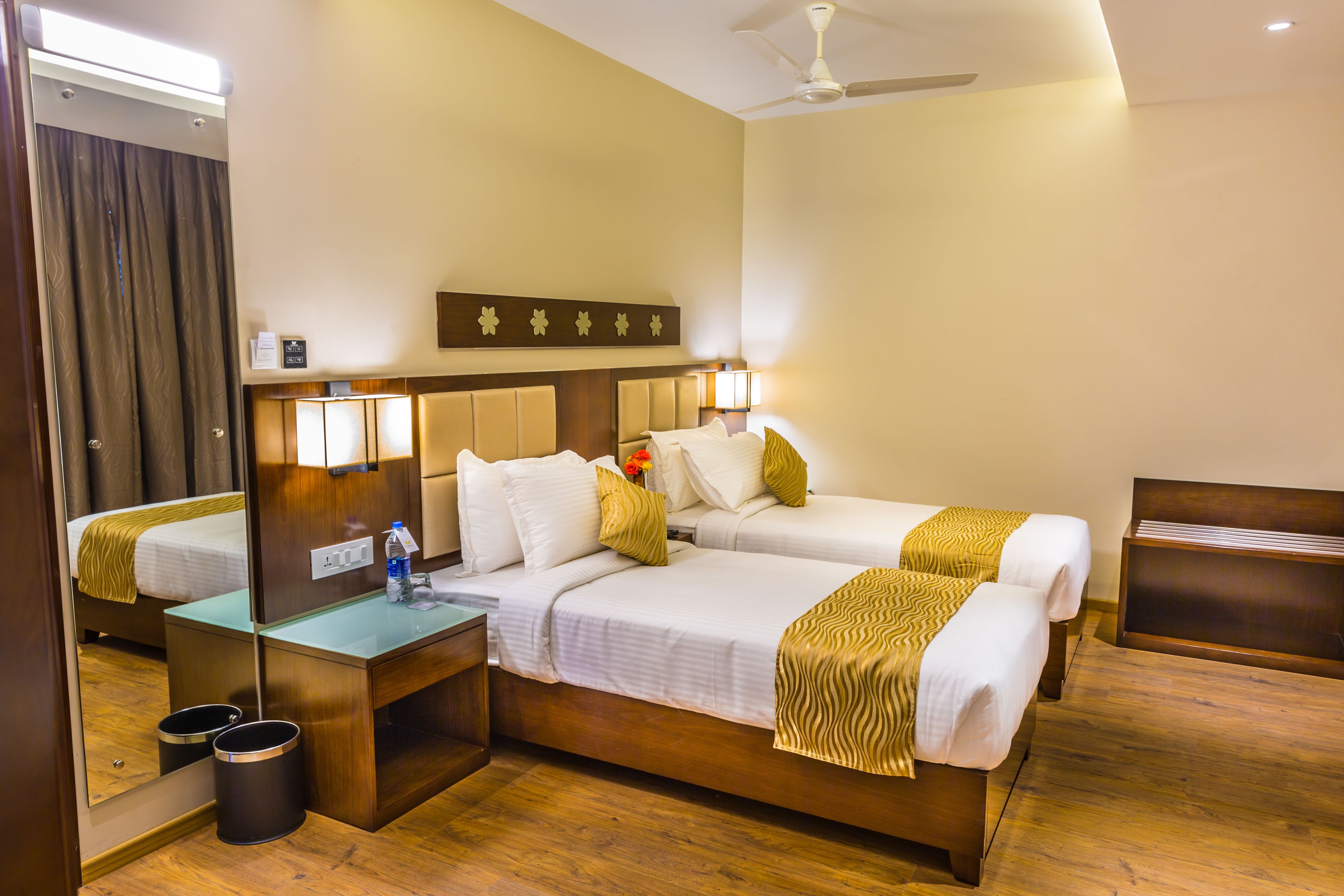 A hotel room with a large bed, a desk, a mirror, and a ceiling fan.
