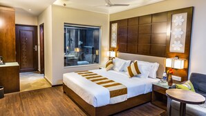 A hotel room with a large bed, a bedside table with a lamp, a chair, a window, and a ceiling fan. - Casa Montana (Devikolam)
