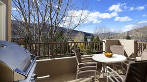 A patio with a grill, a table with chairs, and a view of mountains.