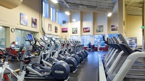 A gym with multiple exercise machines, a clock, and large windows allowing natural light.