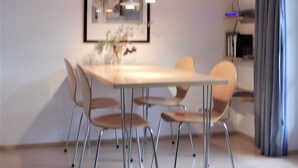 A modern dining area with a long table, multiple chairs, pendant lighting, and a framed picture on the wall. - Holiday apartment on the beach in a traditional thatched-roofed house  (Ostseebad zingst)
