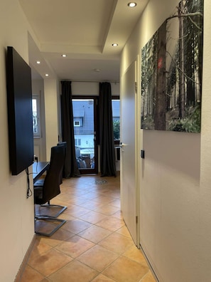 A hallway with a flat-screen TV mounted on the wall, a desk with a chair, and a large painting on the wall. - Designer apartment in the immediate vicinity of the bobsleigh run (Winterberg)