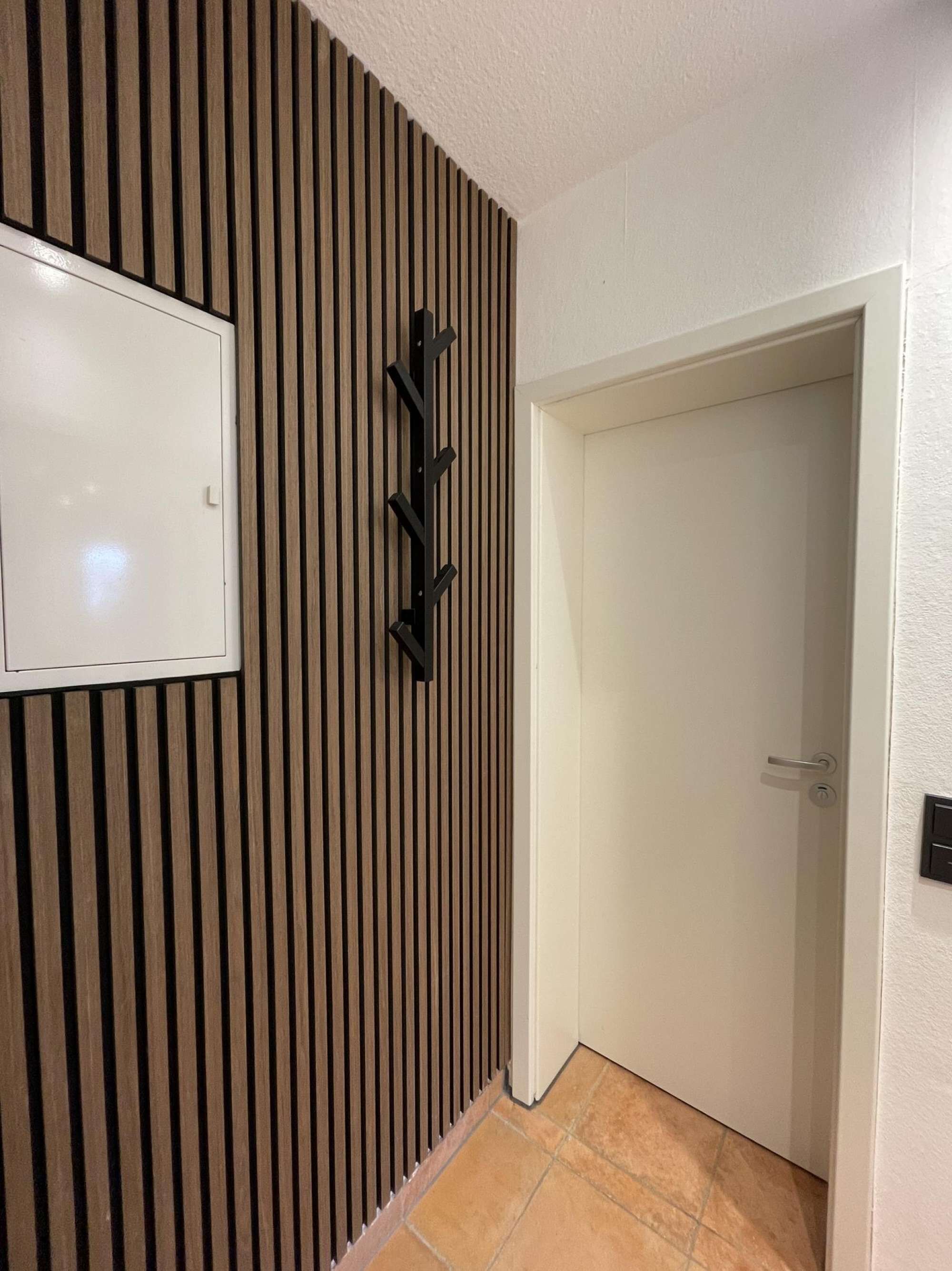A hallway with a wooden slat wall, a white door, and a black wall-mounted rack.