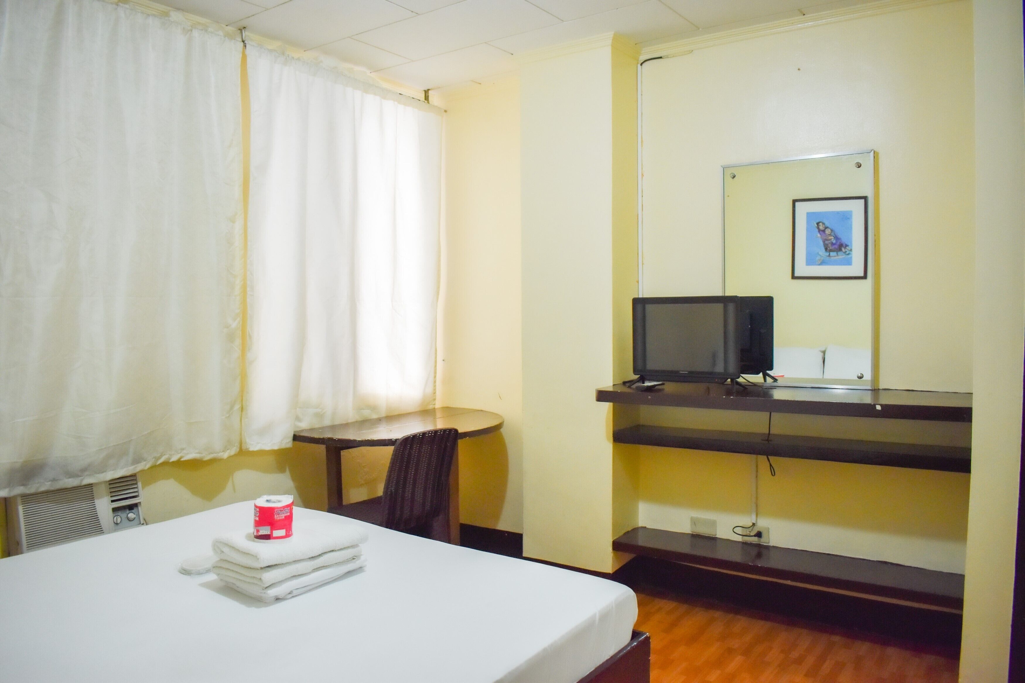 A hotel room with a bed, a desk, a chair, a television, and a picture on the wall.