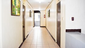 A hotel corridor with doors on both sides, a tiled floor, and a painting on the left wall.