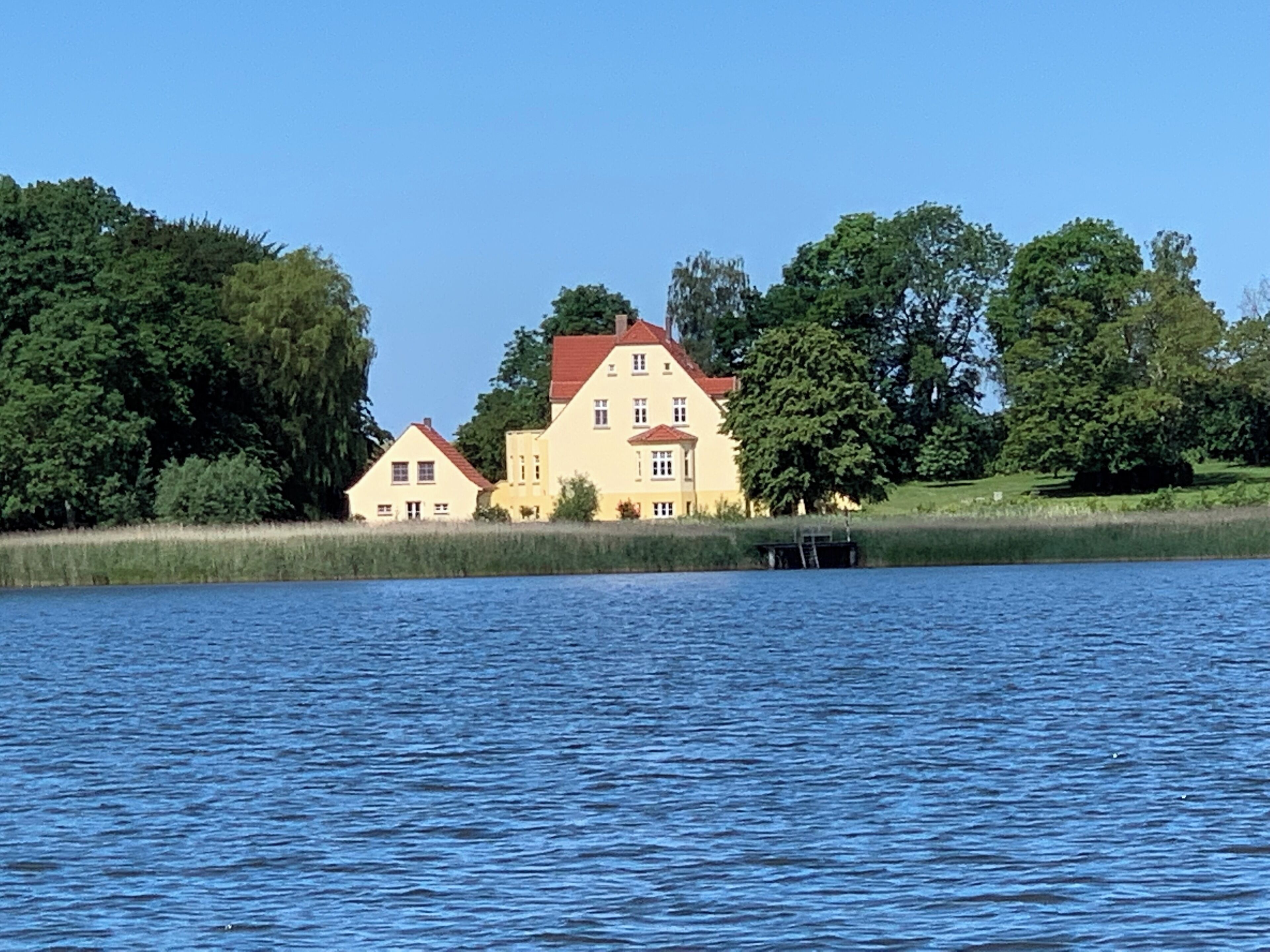 Een vakantiehuis aan het meer met twee hoofdgebouwen, een steiger en veel groen.