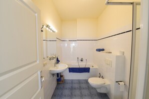 Een bad/douchecombinatie, een haardroger, handdoeken, toiletpapier