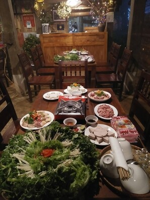 Una mesa de comedor dispuesta con diversos platos, incluyendo carne, verduras y salsas, en un restaurante con mobiliario de madera y un ambiente cálido.