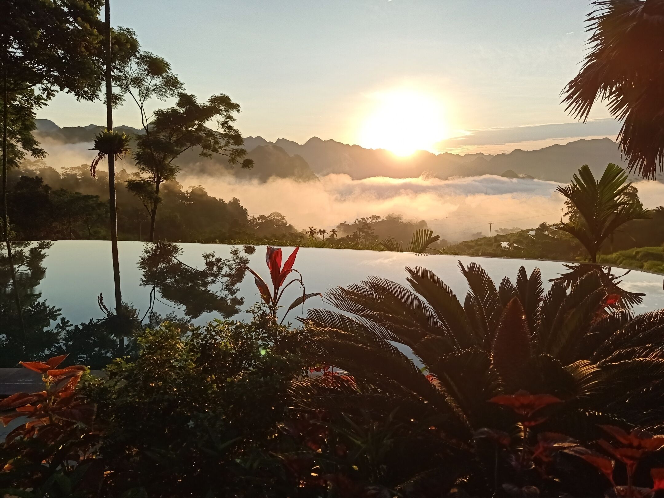 A serene landscape with a clear sky, a body of water reflecting the surroundings, and a mountain range in the distance.