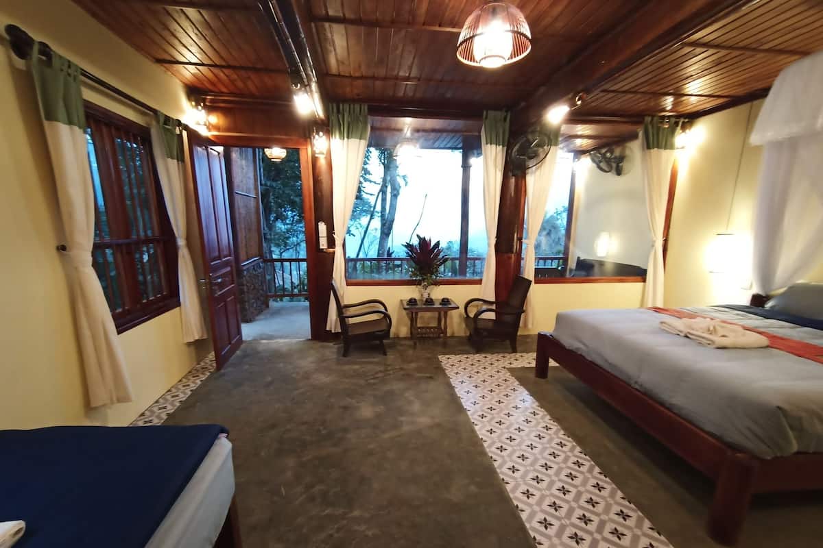 Une chambre avec un lit, un bureau, deux chaises, une fenêtre donnant sur un beau paysage et un ventilateur de plafond.