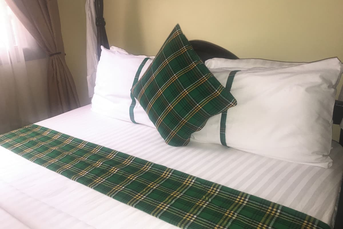 A neatly made bed with white and green plaid bedding, a canopy, and a window with curtains.
