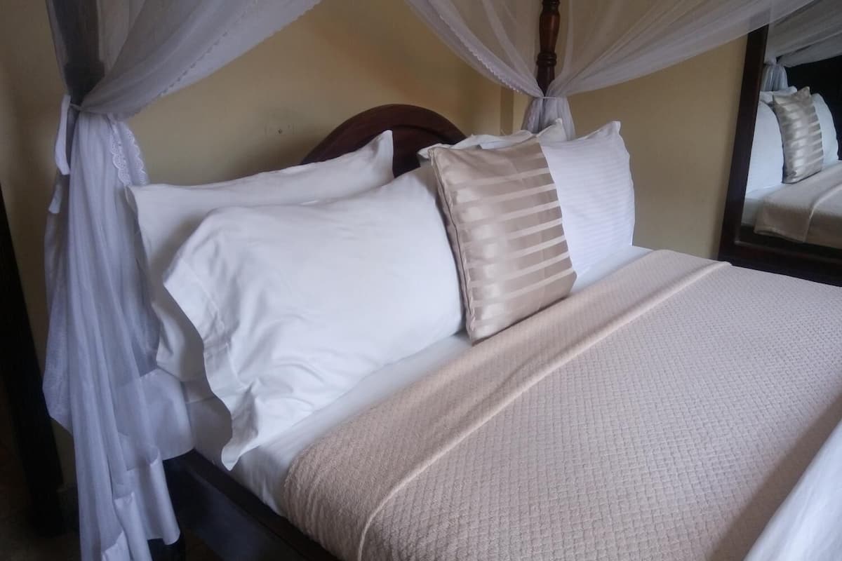 A bed with a canopy, a headboard, and a mirror reflecting part of the room.