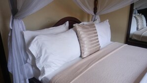 A bed with a canopy, a headboard, and a mirror reflecting part of the room.