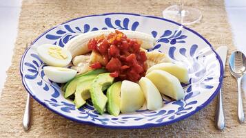 A plate with sliced bananas, avocado, and a tomato-based topping, accompanied by a boiled egg, on a patterned plate.