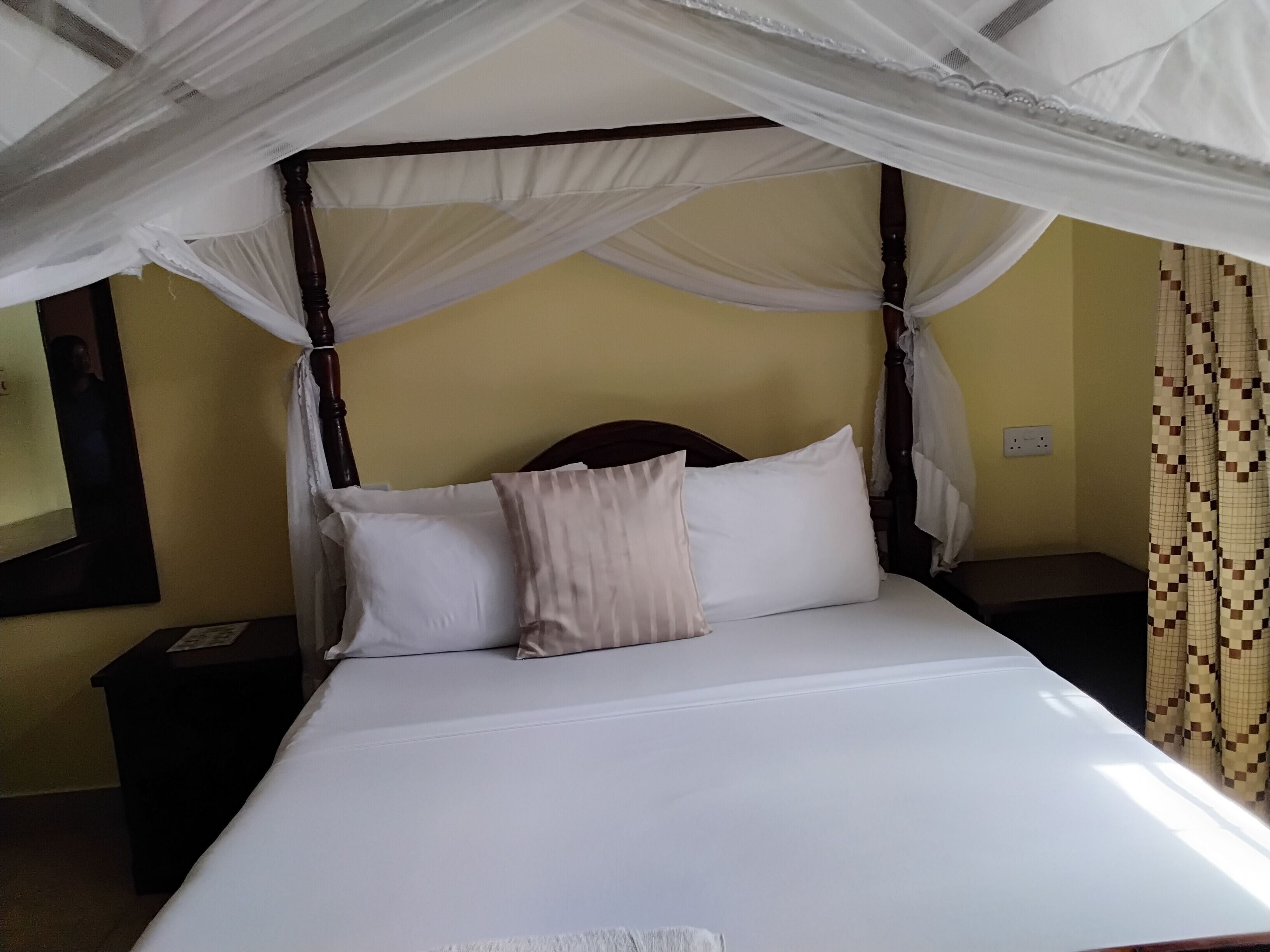 A bed with a canopy, a bedside table, a wall-mounted phone, and a patterned curtain.