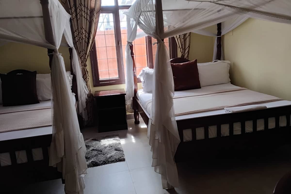 A room with two beds, each with a canopy, a small table, and a view of the outside through a window.