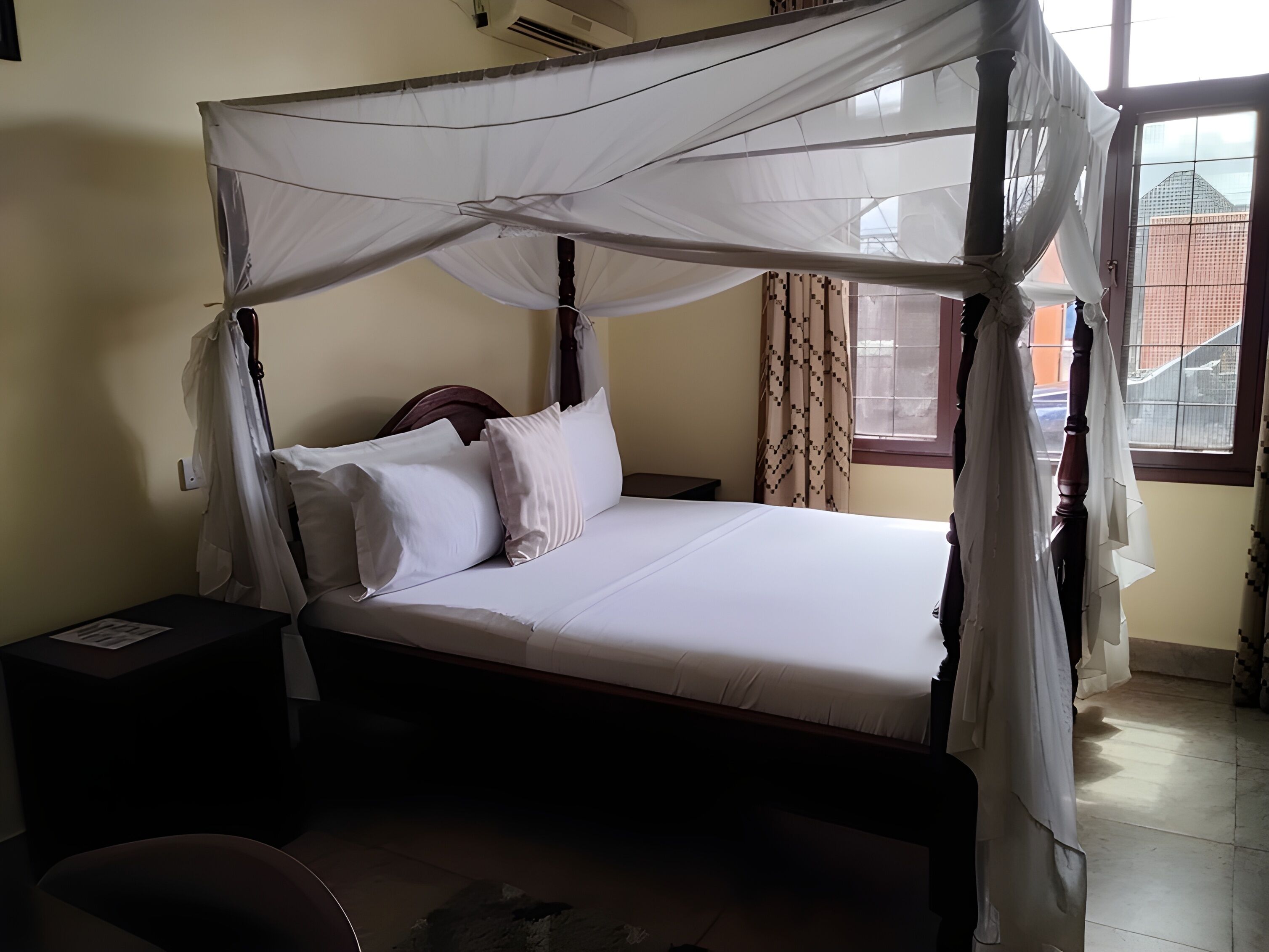 Una cama con dosel, una mesita de noche y una ventana con cortinas.